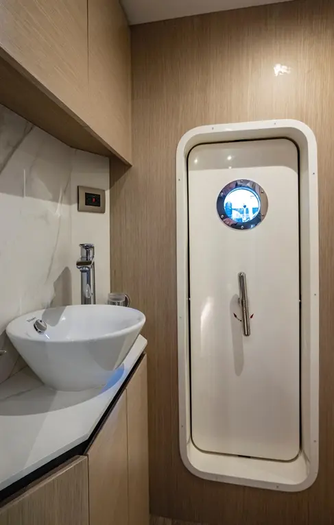 Modern bathroom featuring a white vessel sink, wooden cabinetry, and a unique white door with a circular window.